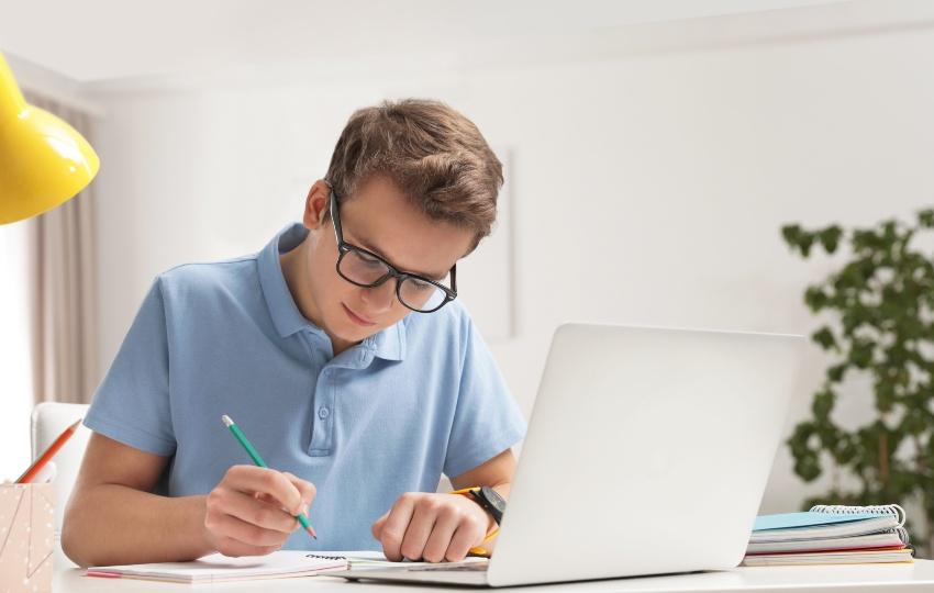 Schüler macht Hausaufgaben, im Vordergrund ein Laptop