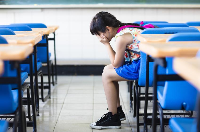 Junge Schülerin sitzt unglücklich alleine im Klassenzimmer - Die frühe Einschulung birgt auch Risiken