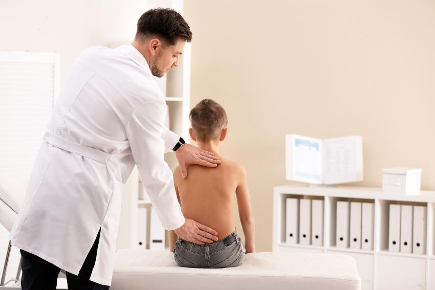 Arzt untersucht den Rücken eines Schülers