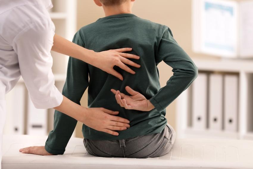 Junge bei Ärztin mit Rückenschmerzen - Haltungsschäden bei Kindern vermeiden
