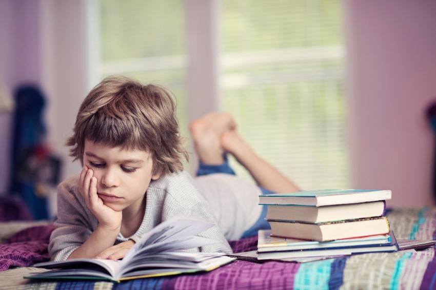 Junge liest Buch im Bett - Konzentration in der Schule fördern durch Entspannung zuhause
