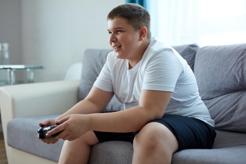 Übergewichtiges Kind sitzt auf der Couch und spielt Playstation
