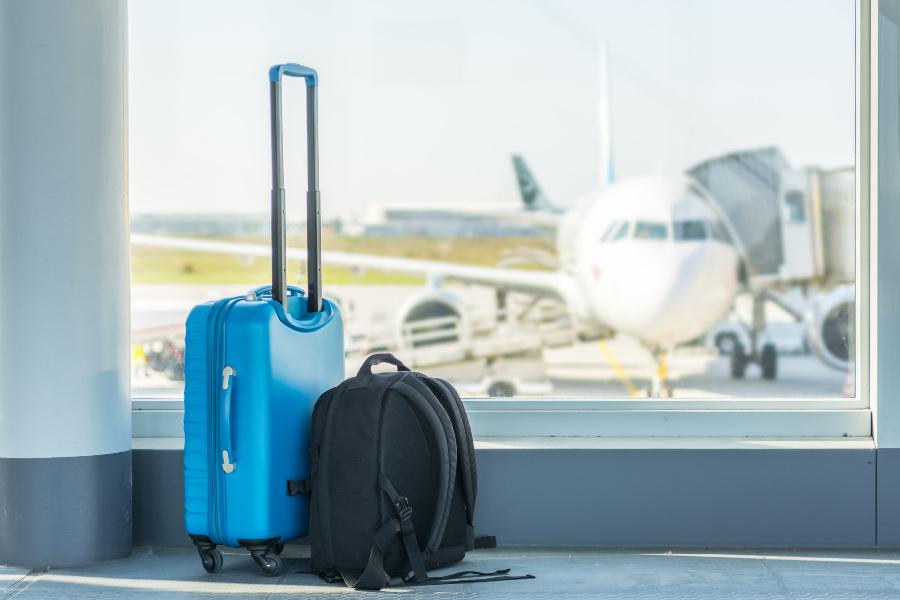 Auf dem Flughafen stehen ein Trolley und ein Rucksack vor einem startbereiten Flieger. Koffer für Flugreisen