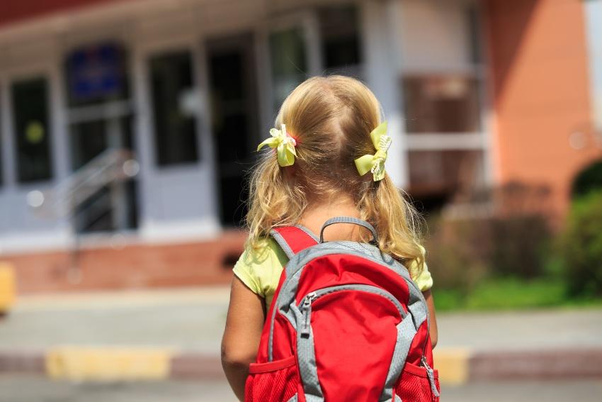 Junges Mädchen mit einem Schulrucksack vor einer Schule