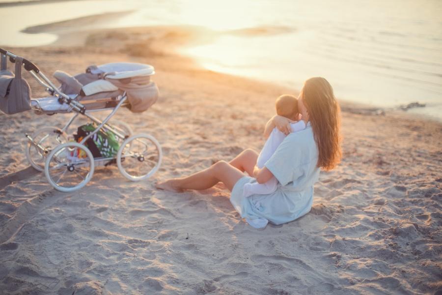 Junge Frau mit Baby am Strand - Wickelrucksäcke für untrwegs